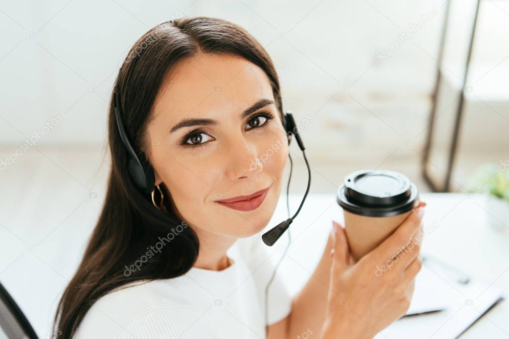 positive broker in headset holding disposable cup in office 