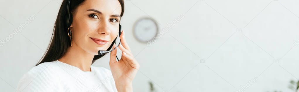 panoramic shot of beautiful broker touching headset while looking at camera 