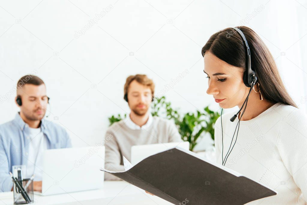 selective focus of attractive broker holding folder near coworkers in office 