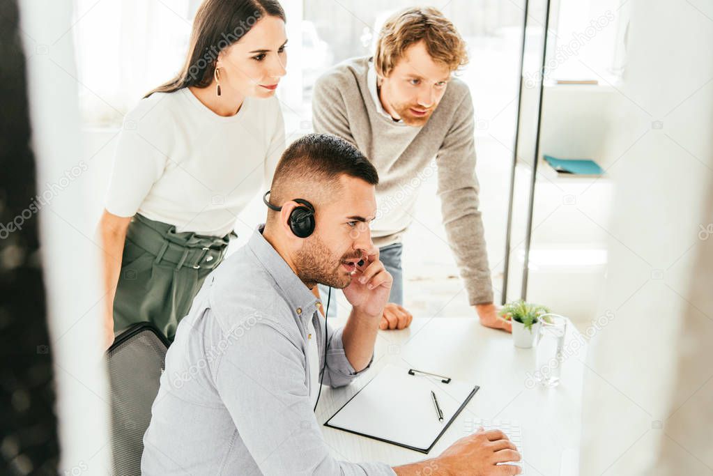 selective focus of broker in headset talking near coworkers in office 