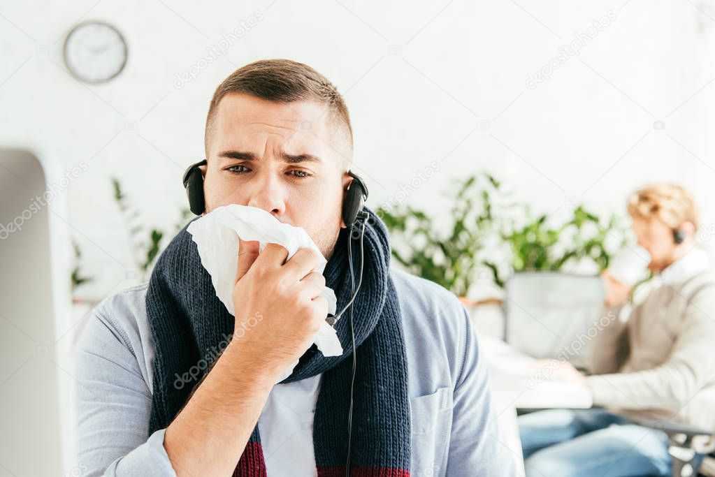 selective focus of sick broker sneezing near coworker in office 