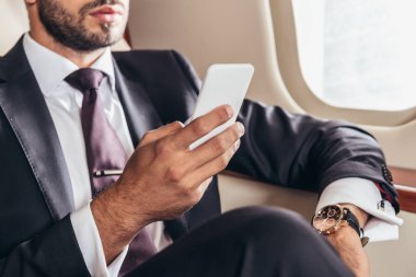 Özel uçakta akıllı telefon kullanan takım elbiseli iş adamının görüntüsü. 