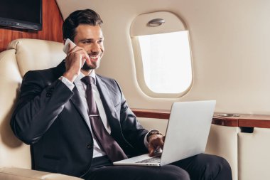 Takım elbiseli gülümseyen iş adamı özel uçakla akıllı telefondan konuşuyor. 