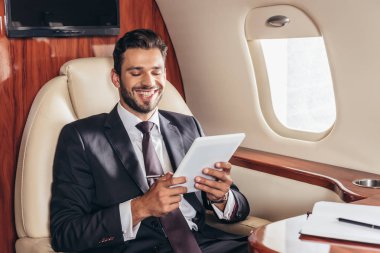 Gülümseyen iş adamı özel uçakta dijital tablet kullanıyor. 