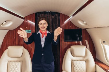 smiling flight attendant in uniform with outstretched hands in private plane  clipart