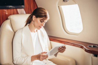 Takım elbiseli çekici iş kadını özel uçakta dijital tablet kullanıyor. 