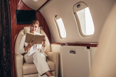 Takım elbiseli çekici bir iş kadını özel uçakta kitap okuyor. 