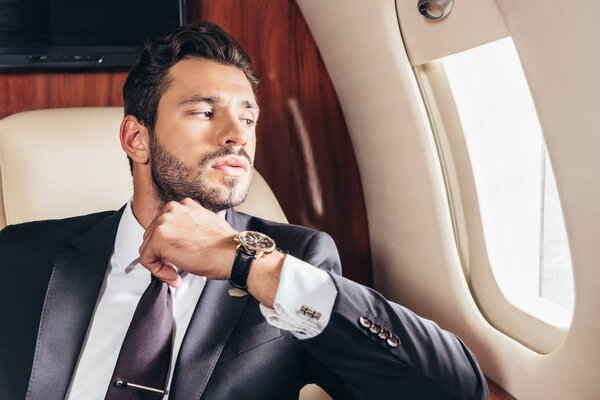handsome businessman in suit looking through window in private plane 