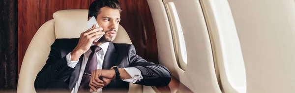 スーツ姿のハンサムなビジネスマンがプライベート飛行機の中でスマートフォンで話をし — ストック写真