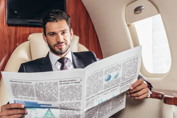 穿着西装的英俊商人在私人飞机上拿着报纸 — 图库照片