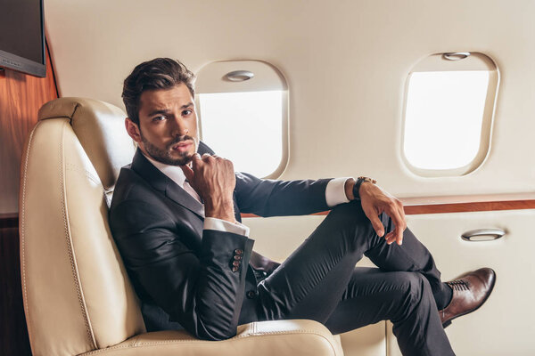 красивый бизнесмен в костюме смотрит в камеру в частном самолете
 