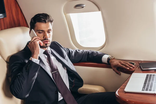 スーツ姿のハンサムなビジネスマンが飛行機の中でスマホで話している — ストック写真