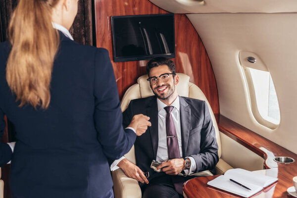 smiling businessman in suit looking at flight attendant in private plane 