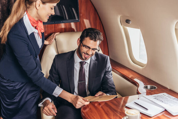 flight attendant giving menu to smiling businessman in suit in private plane 