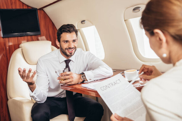 selective focus of businessman looking at businesswoman with contract in private plane 