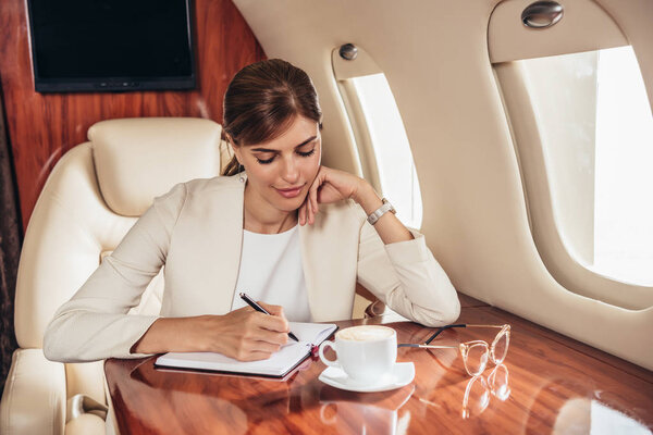 attractive businesswoman in suit writing in notebook in private plane 