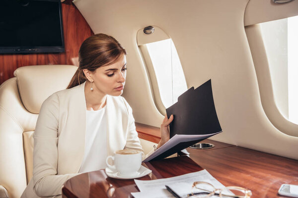 attractive businesswoman in suit doing paperwork in private plane 