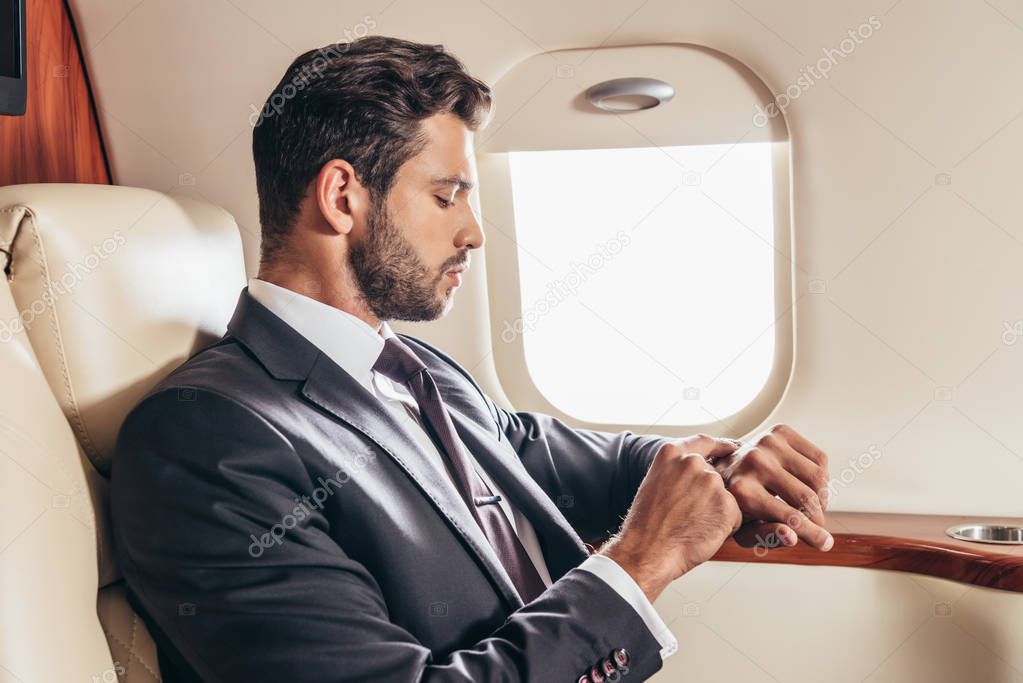 side view of handsome businessman in suit looking at wristwatch in private plane 