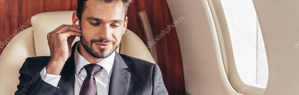 panoramic shot of handsome businessman in suit listening music in private plane 