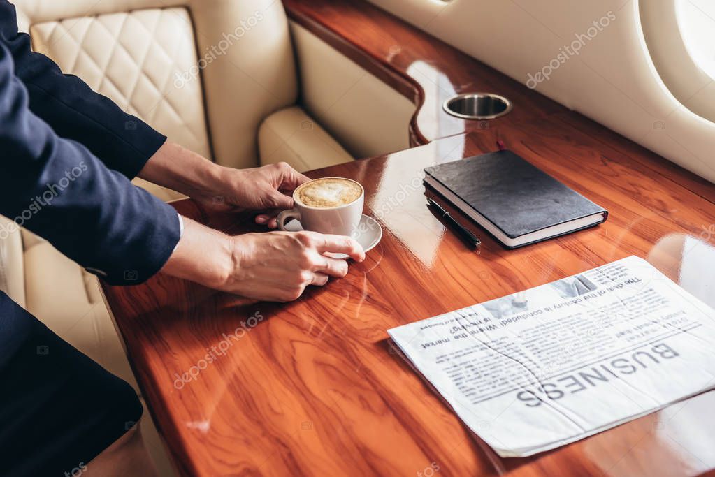 cropped view of flight attendant putting cup of coffee on table in private plane 