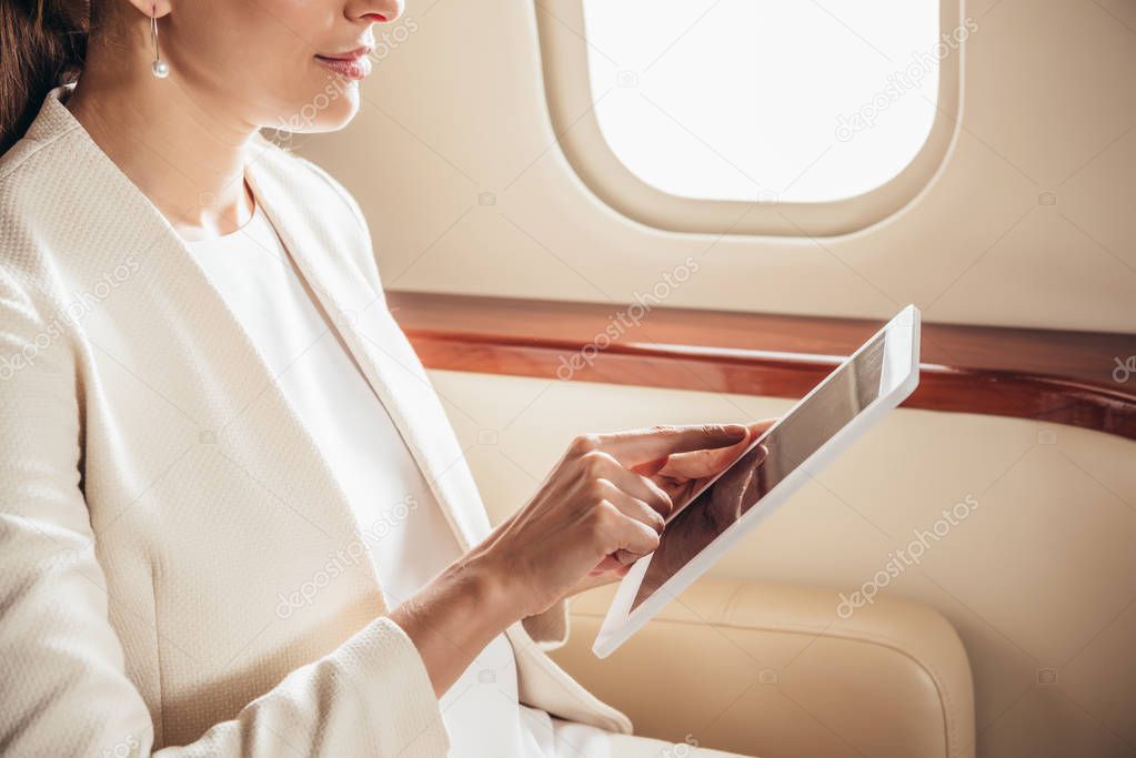 cropped view of businesswoman in suit using digital tablet in private plane 
