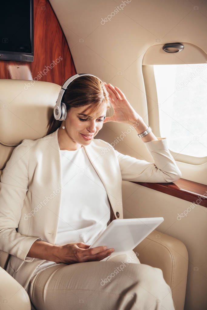 attractive businesswoman in suit listening music and using digital tablet in private plane 