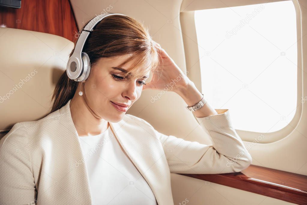 attractive businesswoman in suit listening music with headphones in private plane 