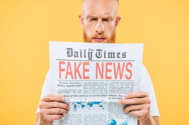 Sahte haberlerle gazete okuyan ciddi bir adamın seçici odak noktası, sarı renkte izole edilmiş.