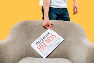 Kırpılmış bir adamın gazeteyi sahte haberlerle sarılı koltuğa koyduğu görüntüsü.