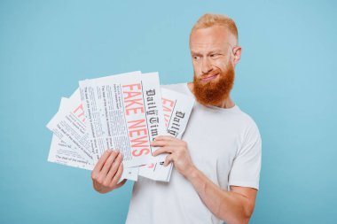 Kuşkucu sakallı adam sahte haberlerle gazetelere bakıyor.