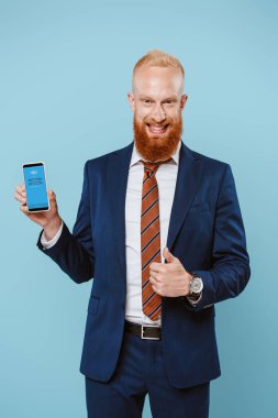 Kyiv, Ukrayna - 27 Ağustos 2019: gülümseyen sakallı iş adamı başparmağını kaldırıyor ve Skype uygulaması ile akıllı telefon kullanıyor.