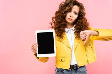 Üzgün kıvırcık kız başparmağını aşağı gösteriyor ve dijital tablet boş ekran ile, pembe üzerine izole edilmiş
