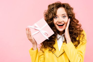 Heyecanlı, çekici, kıvırcık kız hediyesini tutuyor, pembe üzerine izole edilmiş.