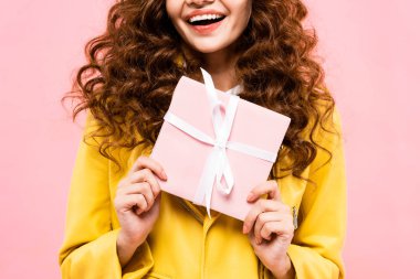 cropped view of curly girl holding gift, isolated on pink clipart