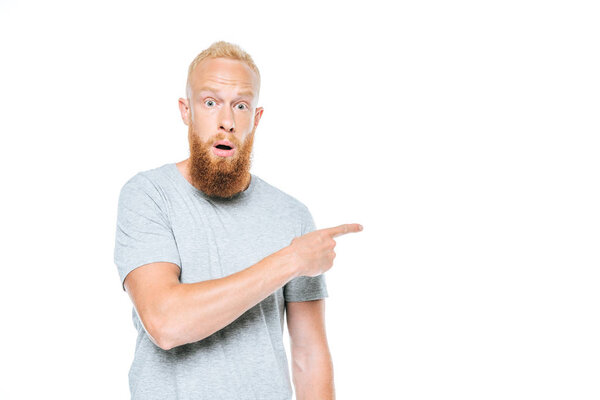 Beautiful bearded shocked man in grey t-shirt pointing isolated on white
