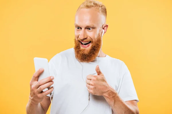 cheerful bearded man with earphones taking selfie on smartphone and showing ok sign, isolated on yellow