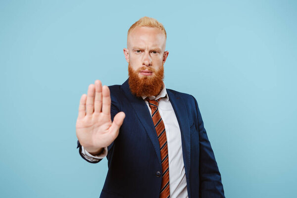 серьезный бизнесмен в костюме показывая знак "стоп", изолированный на синий
