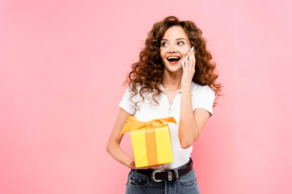 Excited Curly Girl Holding Gift Box Talking Smartphone Isolated Pink — Stock Photo, Image