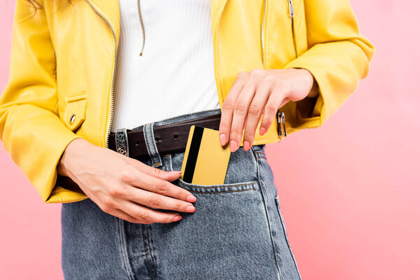 cropped view of girl putting credit card into pocket, isolated on pink