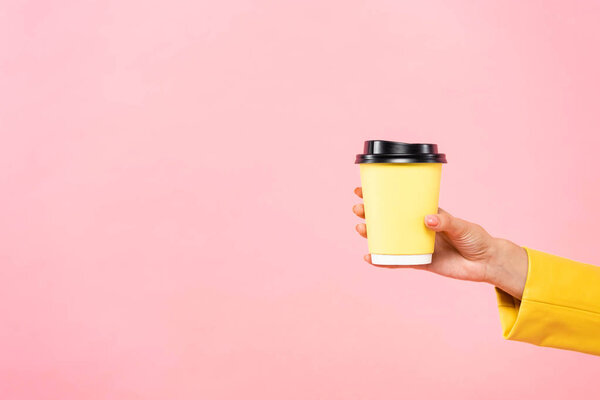 cropped view of woman holding yellow disposable cup of coffee, isolated on pink