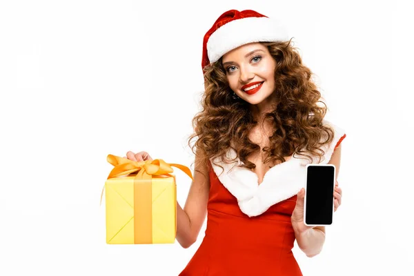 身穿桑塔服装的迷人的微笑女孩 手里拿着圣诞礼物和带有空白屏幕的智能手机 与白色隔离 — 图库照片