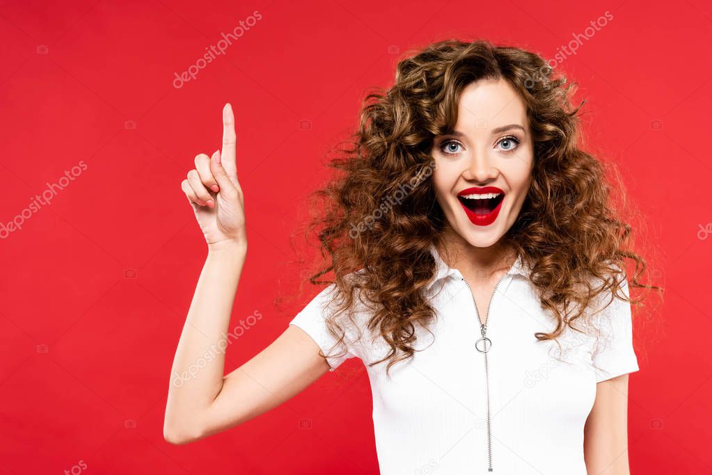 excited attractive curly girl pointing up isolated on red