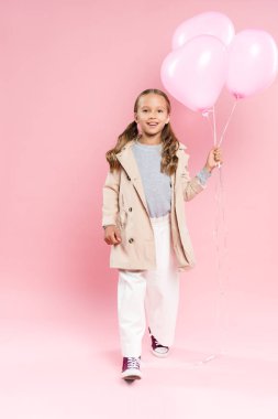 Sonbahar kıyafetli gülümseyen çocuk pembe arka planda balonlar tutuyor. 