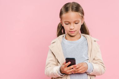 Sonbahar kıyafetli şirin çocuk pembe üzerine izole edilmiş akıllı telefon kullanıyor.