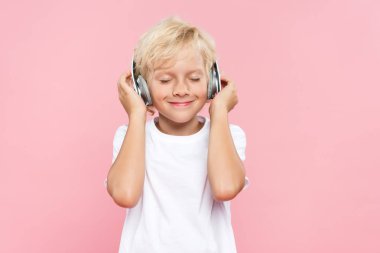 Kulaklıklı gülümseyen çocuk pembe renkte müzik dinliyor.