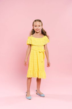 Gülümseyen ve sevimli bir çocuk pembe arka planda kameraya bakıyor. 