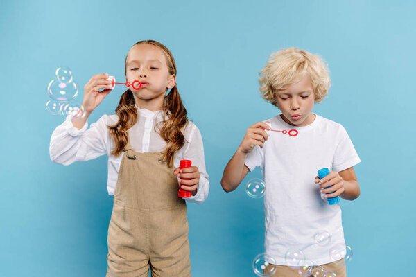 cute kids holding bottles and blowing soap bubbles on blue background 