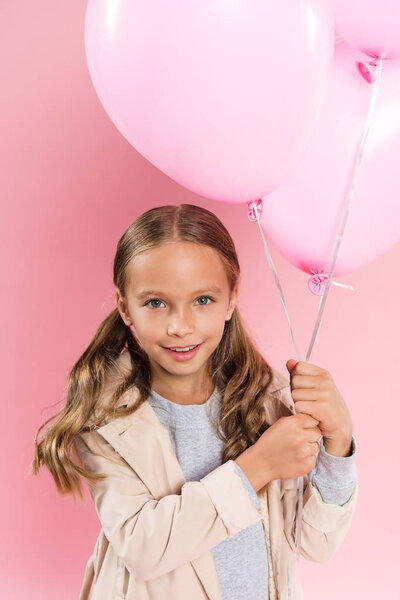 high angle view of smiling kid in autumn outfit holding balloons on pink background 
