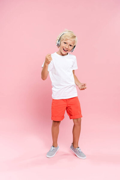 smiling kid with headphones listening music and dancing on pink background 