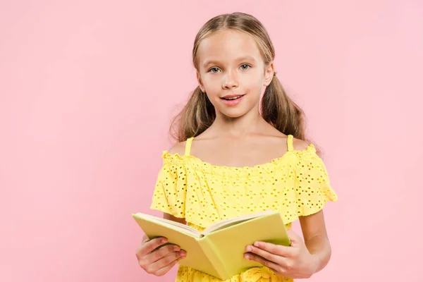 Улыбающийся Ребенок Держит Книгу Смотрит Камеру Изолированную Розовый — стоковое фото